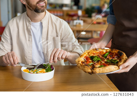 Client getting his pizza in pizzeria and looking contented Client getting his pizza in pizzeria and looking contented 127631043