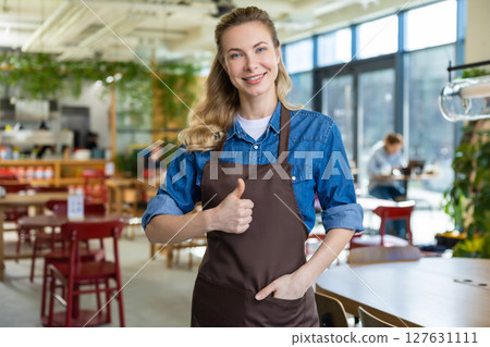 Pretty blonde woman in apron looking happy at her working place in pizzeria Pretty blonde woman in apron looking happy at her working place in pizzeria 127631111