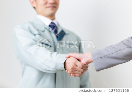 一位穿西裝的女商人和一位穿著工作服的商人握手 一位穿西裝的女商人和一位穿著工作服的商人握手 127631166