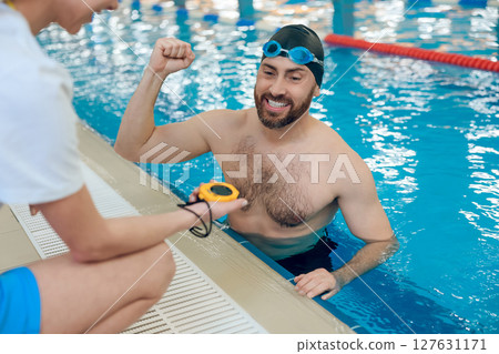Man having a workout in the swimming pool and talking with his coach Man having a workout in the swimming pool and talking with his coach 127631171
