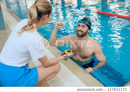Man having a workout in the swimming pool and talking with his coach Man having a workout in the swimming pool and talking with his coach 127631172