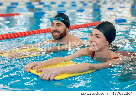 Young cute couple in swimming with boards in the pool 127631204