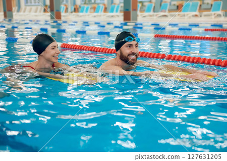 Young cute couple in swimming with boards in the pool Young cute couple in swimming with boards in the pool 127631205