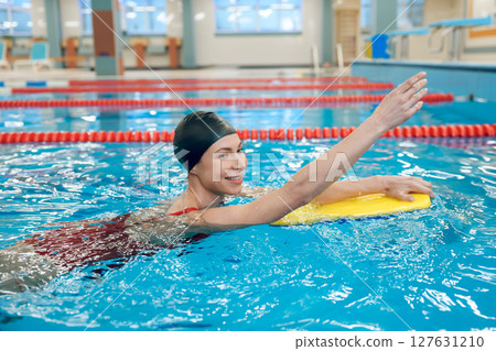 Cute caucasian young woman swimming in the pool with a board Cute caucasian young woman swimming in the pool with a board 127631210