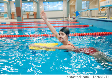 Cute caucasian young woman swimming in the pool with a board 127631212