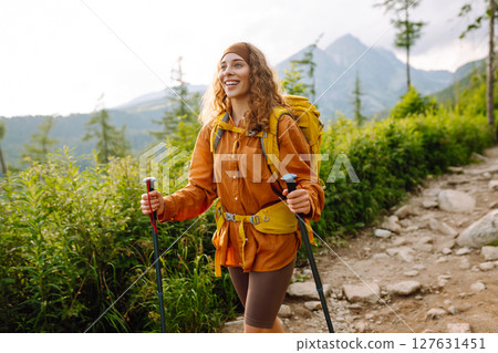 Young woman traveler hiking poles on trail among the mountains. Hiking. Active lifestyle. Young woman traveler hiking poles on trail among the mountains. Hiking. Active lifestyle. 127631451