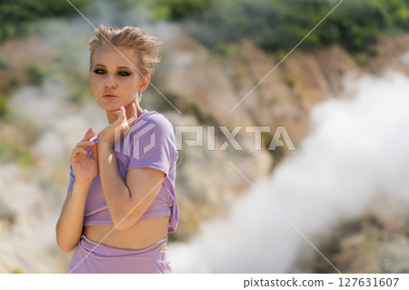 Fashion model looking at camera, standing against backdrop of volcano crater, with clouds of gas, pair of steaming geysers in background. Nature's beauty, plenty of copy space to add creative ideas Fashion model looking at camera, standing against backdrop of volcano crater, with clouds of gas, pair of steaming geysers in background. Nature's beauty, plenty of copy space to add creative ideas 127631607