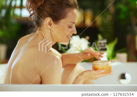 Woman Pampering Skin with Body Scrub in Bath Woman Pampering Skin with Body Scrub in Bath 127632554