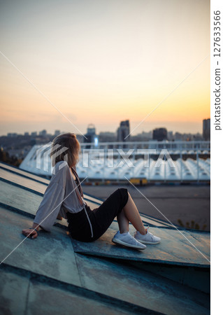 Beautiful woman on rooftop posing at sunset. Woman enjoys atmosphere of city of freedom. Relaxation. 127633566