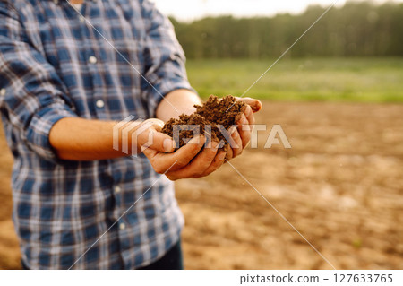 Farmer's hands take the soil from field and check its quality. Experienced male hands hold the soil. 127633765