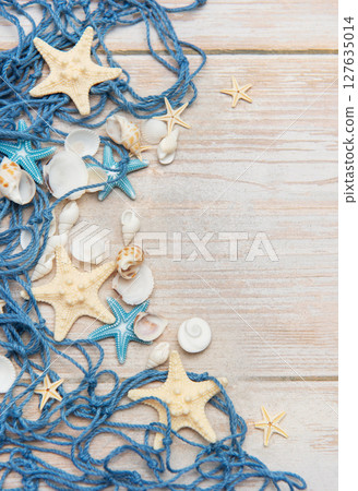 Fishing net, starfishes and seashells lying on wooden planks background 127635014