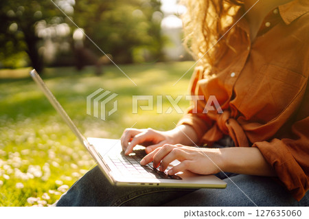 Portrait of a happy woman in sunny park on green lawn with a laptop. Freelance concept, technology. 127635060