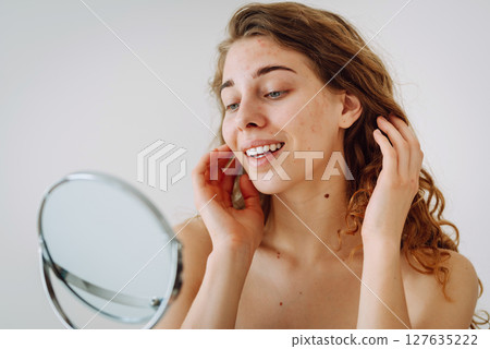 Beautiful woman with problematic skin looks in her small mirror. Cosmetology. Skin care concept. Beautiful woman with problematic skin looks in her small mirror. Cosmetology. Skin care concept. 127635222