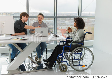 Teamwork brainstorm. Diverse multiracial colleagues woman in chair for people with disability working together. Group of people sitting in creative office discussing business. Young professional team Teamwork brainstorm. Diverse multiracial colleagues woman in chair for people with disability working together. Group of people sitting in creative office discussing business. Young professional team 127635246