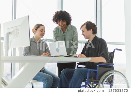 Teamwork brainstorm. Diverse multiracial colleagues man in chair for people with disability working together. Group of people sitting in creative office discussing business. Young professional team 127635270