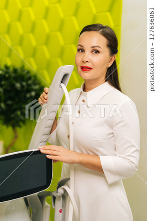 Vertical portrait of cosmetologist posing with new modern mesotherapy apparatus, holding handles, showcasing professional equipment for advanced skincare treatments, looking at camera. Vertical portrait of cosmetologist posing with new modern mesotherapy apparatus, holding handles, showcasing professional equipment for advanced skincare treatments, looking at camera. 127636061