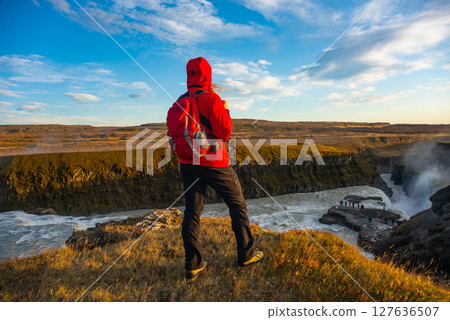 Adventurer stands triumphantly near a stunning Icelandic waterfall Gullfoss. Surrounded by rugged terrain, the person embraces the breathtaking natural beauty and vibrant rushing waters Adventurer stands triumphantly near a stunning Icelandic waterfall Gullfoss. Surrounded by rugged terrain, the person embraces the breathtaking natural beauty and vibrant rushing waters 127636507