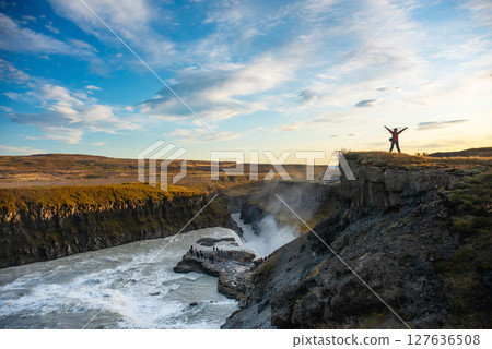 Adventurer stands triumphantly near a stunning Icelandic waterfall Gullfoss. Surrounded by rugged terrain, the person embraces the breathtaking natural beauty and vibrant rushing waters Adventurer stands triumphantly near a stunning Icelandic waterfall Gullfoss. Surrounded by rugged terrain, the person embraces the breathtaking natural beauty and vibrant rushing waters 127636508