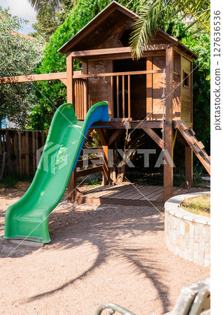 Wooden playground with treehouse and slide in a sunny garden. Outdoor fun, nature play, and childhood adventure concept. 127636536