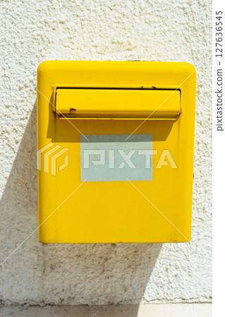Yellow mailbox on bright white wall. Postal service, communication symbol, and street detail in sunny environment. Yellow mailbox on bright white wall. Postal service, communication symbol, and street detail in sunny environment. 127636545