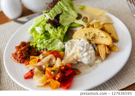 Plate with salad, roasted vegetables, potatoes, and cheese on dining table close-up. Healthy lunch option, balanced nutrition, and hotel meal concept. 127636593