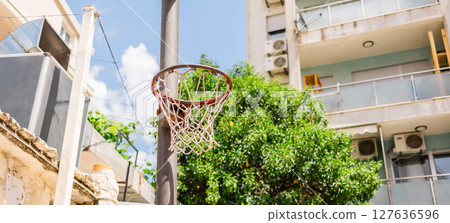 Old basketball hoop in urban courtyard under the summer sky, banner with copy space. Concept of street sports, childhood memories, and outdoor recreation in residential neighborhoods. Old basketball hoop in urban courtyard under the summer sky, banner with copy space. Concept of street sports, childhood memories, and outdoor recreation in residential neighborhoods. 127636596