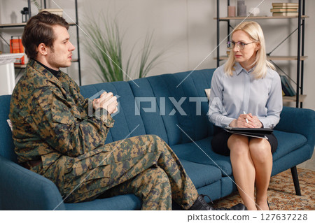 Soldier and psychiatrist sitting on couch during therapy session. Man wearing military uniform. Male warrior with ptds talking to psychiatrist. 127637228