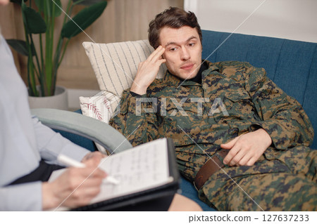 Soldier laying on couch during therapy session. Man wearing military uniform. Male warrior with ptds talking to psychiatrist. 127637233
