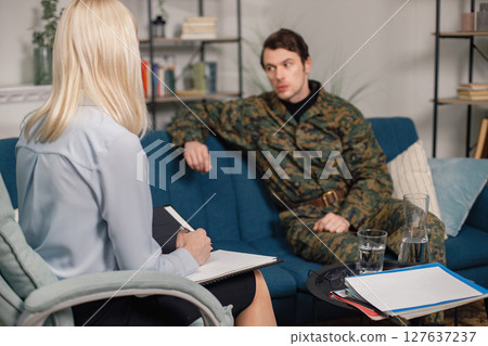 Soldier and psychiatrist sitting on couch during therapy session. Man wearing military uniform. Male warrior with ptds talking to psychiatrist. 127637237