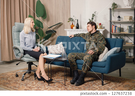 Soldier and psychiatrist sitting on couch during therapy session. Man wearing military uniform. Male warrior with ptds talking to psychiatrist. 127637238