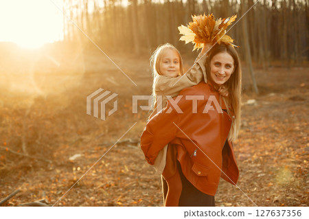 Fashionable mother with daughter. Family in a autumn park. Little daughter in a brown coat. 127637356