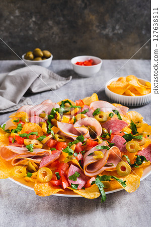 Charcuterie nachos with chips, salami, cheese and olives on a plate on a table vertical view 127638511