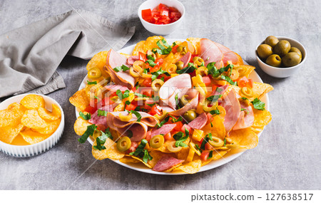 Charcuterie nachos with chips, salami, cheese and olives on a plate on a table web banner 127638517