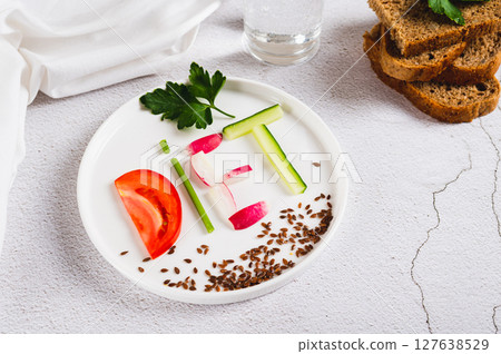 The word diet from vegetables on a plate, bread and a glass of water on the table 127638529
