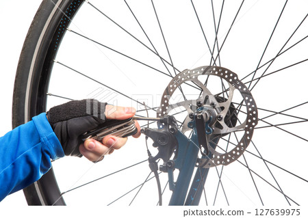 A cyclist in a adjusts a bicycle disc brake with a multi-tool, focusing on the wheel's roto A cyclist in a adjusts a bicycle disc brake with a multi-tool, focusing on the wheel's roto 127639975