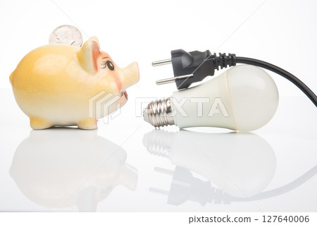 Piggy bank, LED lamp and electric cable plug. Saving electricity. Energy saving concept 127640006