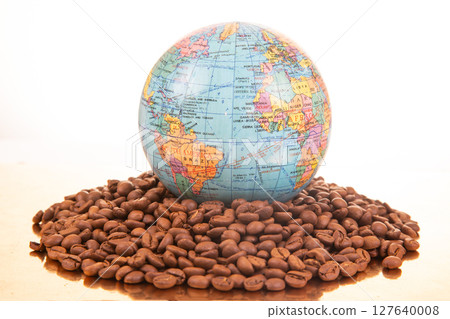 A colorful globe rests on a pile of roasted coffee beans against a white background 127640008
