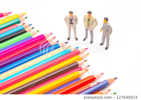An assortment of vivid colored pencils lies beside three small business figurines An assortment of vivid colored pencils lies beside three small business figurines 127640015