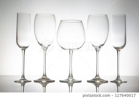 A sleek lineup of five elegant, empty wine glasses with long stems, reflecting on a glossy surface A sleek lineup of five elegant, empty wine glasses with long stems, reflecting on a glossy surface 127640017