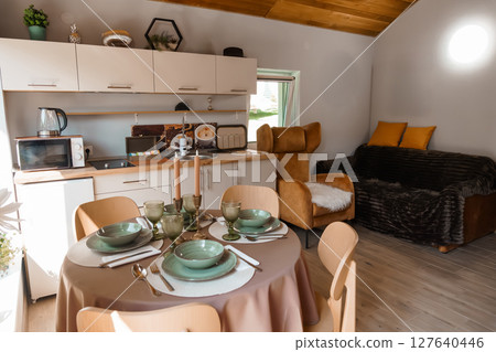 Cozy Cabin Kitchen Dining Area Interior with Modern Appliances, Beige Decor, Warm Lighting, Comfortable Seating, Small Space Living, Rustic Style. Cozy Cabin Kitchen Dining Area Interior with Modern Appliances, Beige Decor, Warm Lighting, Comfortable Seating, Small Space Living, Rustic Style. 127640446