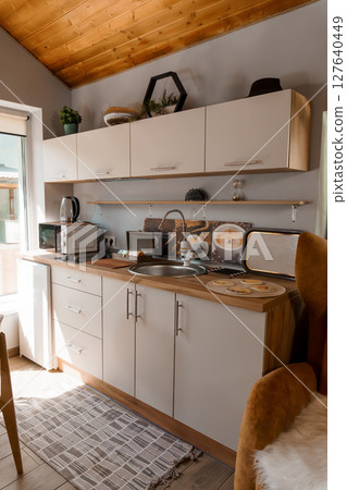 Cozy Small Kitchen Interior with Wooden Accents, Beige Cabinets, and Gray Floor Tiles: Rustic Home Design, Breakfast Scene, Natural Light 127640449