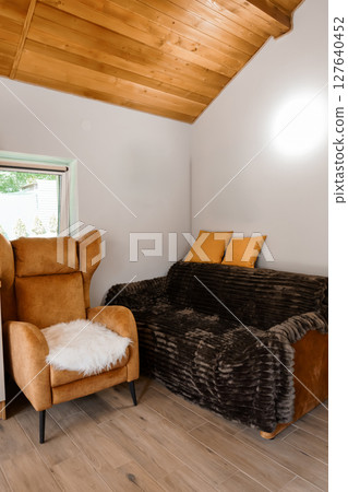 Cozy Rustic Living Room Interior with Brown Leather Armchair, Faux Fur Sofa, Wood Ceiling, Warm Lighting, and Comfortable Seating Arrangement. Cozy Rustic Living Room Interior with Brown Leather Armchair, Faux Fur Sofa, Wood Ceiling, Warm Lighting, and Comfortable Seating Arrangement. 127640452