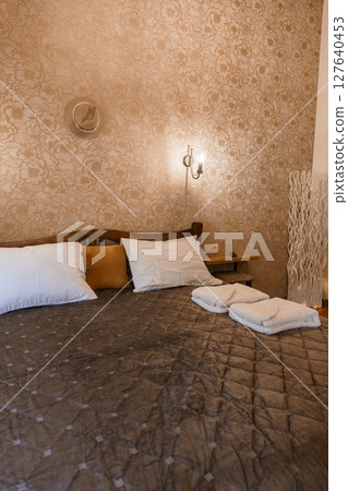 Luxurious Bedroom Interior with Beige Floral Wallpaper, Brown Bedding, Wall Sconce Lighting, and Elegant Decorative Elements Luxurious Bedroom Interior with Beige Floral Wallpaper, Brown Bedding, Wall Sconce Lighting, and Elegant Decorative Elements 127640453