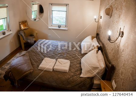 Cozy Bedroom Interior Design Featuring a Large Bed, Neutral Colors, Wall Sconces, and Rustic Accents, Warm Lighting, and Decorative Textiles. Cozy Bedroom Interior Design Featuring a Large Bed, Neutral Colors, Wall Sconces, and Rustic Accents, Warm Lighting, and Decorative Textiles. 127640454