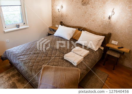 Cozy Bedroom Interior with King Bed, Wall Sconces, Wooden Furniture, and Patterned Wallpaper in Warm Earth Tones - Relaxing Atmosphere Cozy Bedroom Interior with King Bed, Wall Sconces, Wooden Furniture, and Patterned Wallpaper in Warm Earth Tones - Relaxing Atmosphere 127640456
