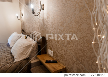 Cozy Bedroom Interior with Floral Wallpaper and Warm Lighting: A Relaxing Scene Featuring a Bedside Table, Sconces, and Decorative Lights Cozy Bedroom Interior with Floral Wallpaper and Warm Lighting: A Relaxing Scene Featuring a Bedside Table, Sconces, and Decorative Lights 127640458