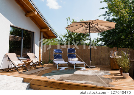 Modern Outdoor Patio Scene with Beige Umbrella, Lounge Chairs, and Wooden Deck Featuring a Relaxing Summer Atmosphere 127640470