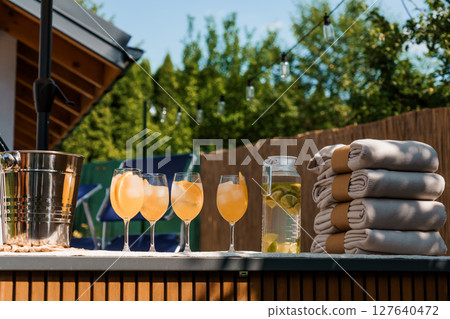 Luxurious Outdoor Summer Party Scene with Cocktails, Towels, and Bar Setup on a Sunny Patio with Wooden Fence. Luxurious Outdoor Summer Party Scene with Cocktails, Towels, and Bar Setup on a Sunny Patio with Wooden Fence. 127640472