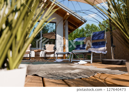 Serene Outdoor Patio Relaxation Scene Featuring Wooden Deck, Lounge Chairs, and a Cozy Garden View Under a Bright Sunny Sky 127640473