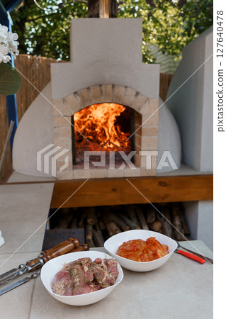 Outdoor Stone Pizza Oven with Burning Wood Fire, Grilled Meat, and Dishes, Rustic Patio Setting, Warm Lighting 127640478